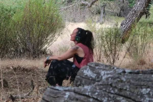 Laura sentada en el bosque con auriculares.